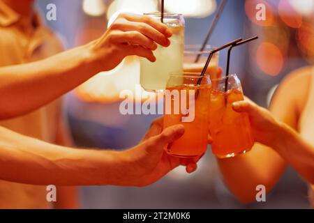 Nahaufnahme von weiblichen und männlichen Händen, die Gläser mit Cocktails mit Eis halten und auf sie klicken. Freunde machen einen festlichen Toast mit köstlichen Zitrusgetränken Stockfoto