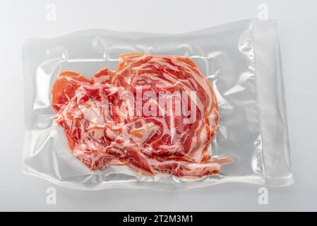 Dünne Speckscheiben in Vakuumverpackung für Sous-Vide-Kochen isoliert mit Schnittpfad im Lieferumfang enthalten Stockfoto