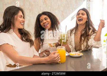 Drei lateinische Freunde genießen gesunde Snacks und Säfte in einer Cafeteria Stockfoto