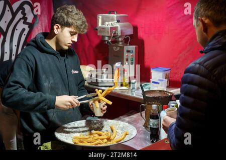 Männliche, die lockige Churros mit Schokoladensauce in einer Tasse serviert werden, frisch zubereitet im Wok an einem Weihnachtsmarkt-Stand in Harrogate, Yorkshire, Großbritannien. Stockfoto