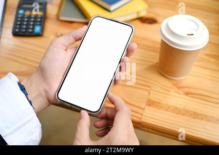 Kopfschuss, Geschäftsmann, der sein Handy benutzt, Informationen oder E-Mails auf dem Telefonbildschirm an seinem Schreibtisch liest. Weißes Mockup des Telefons. Stockfoto