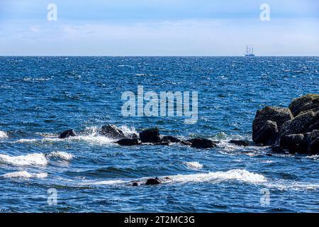 Wellen brechen auf Felsen mit dem Barquentine „Thalassa“ (erbaut 1980) vor der Küste der Kintyre Peninsula, Argyll & Bute, Schottland Großbritannien Stockfoto