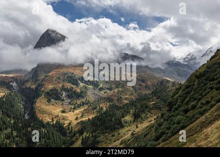 Wolken umgeben die Berghänge des Hangerer über den Kiefernwäldern im Gurglertal im Herbst, Ötztaler Alpen, Tirol, Österreich Stockfoto