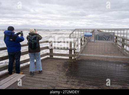 Binz, Deutschland. Oktober 2023. Touristen stehen am Pier im Wind. Aufgrund eines Sturmtief wurden die ersten Straßen und Uferbereiche an der Ostseeküste von Hochwasser überflutet. So waren am Morgen in Wismar sowie in Kiel und Flensburg zahlreiche Straßen und Plätze unter Wasser. Quelle: Stefan sauer/dpa/Alamy Live News Stockfoto