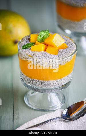 Köstlicher veganer Mango-Chia-Pudding mit frischen Minzquellen in einem Glas auf grünem Holzhintergrund. Selektiver Fokus mit unscharfem Hintergrund. Stockfoto