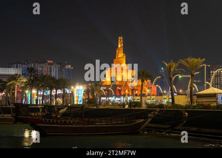 Doha, Katar - 3. Dezember 2022: Traditionelle hölzerne Dhow vor Anker im Dhow Harbor in der Doha Bay mit Spiralmoschee und Minarett im Hintergrund. Blick von vorne Stockfoto