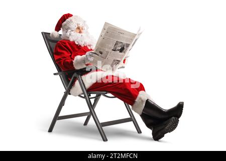 weihnachtsmann sitzt in einem klappbaren Stuhl und liest eine Zeitung isoliert auf weißem Hintergrund Stockfoto