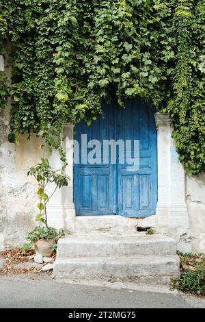 Alte Tür auf der griechischen Insel Kreta im Sommer mit Kriechern bedeckt, traditionelle ländliche Architektur in Griechenland Stockfoto
