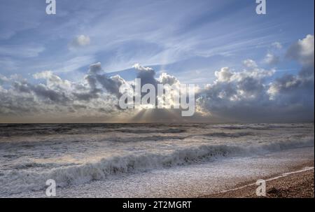 Stürmischer Sonnenuntergang über dem Meer mit blauem Himmel, weißen Wellen und Kieselstrand in Milford on Sea, Hampshire, Großbritannien Stockfoto