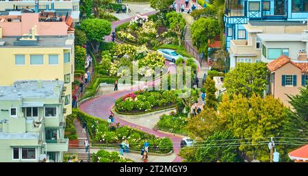 Zoomte in die Luft von Menschen, die die Lombard Street mit silbernem Auto befahren, das die kurvenreiche Straße entlang fährt Stockfoto