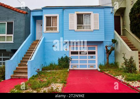 Himmelblaues Haus mit weißen Blenden und Tür mit roter Einfahrt und Gehweg, der die Treppe hinaufführt Stockfoto