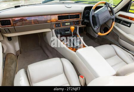 Cockpit eines Jaguar XJS Cabriolets mit Verdeck nach unten auf einem Schotterparkplatz auf dem Land Stockfoto