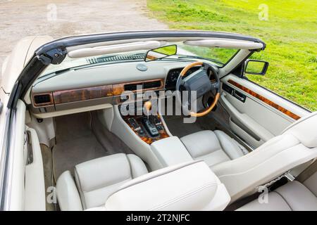 Cockpit eines Jaguar XJS Cabriolets mit Verdeck nach unten auf einem Schotterparkplatz auf dem Land Stockfoto