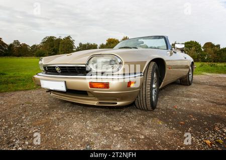 Niedriger Blickwinkel auf den vorderen Abseitenflügel eines Jaguar XJS Cabriolets mit Top-Down-Ansicht auf einem Schotterparkplatz auf dem Land Stockfoto