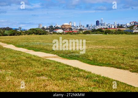 Schotterpfad durch grasbewachsenes Feld und Skyline mit der Rotunde des Palace of Fine Arts und den Wolkenkratzern der Stadt Stockfoto