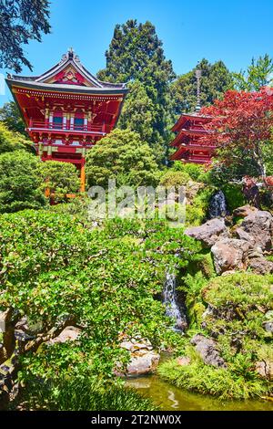 Mini-Wasserfall, der in Knarren mit zwei roten Pagoden auf dem Hügel über dem japanischen Teegarten fließt Stockfoto