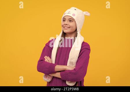 drücken Sie positive Emotionen aus. Glückliches Kind mit Ohrenschützenmütze. Das Kind trägt warme Kleidung auf gelbem Hintergrund. Wintermode und -Schönheit für Kinder. Teenager in Strick Stockfoto