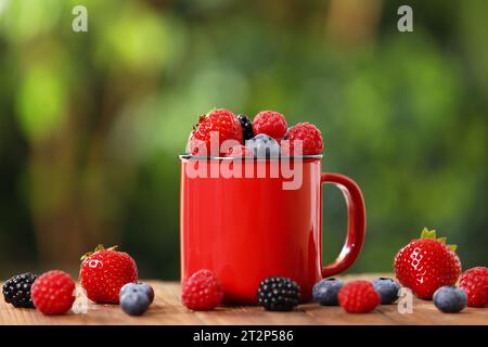 Becher mit verschiedenen frischen, reifen Beeren auf einem Holztisch im Freien Stockfoto