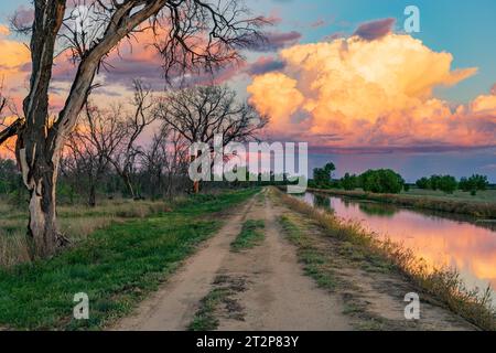 Eine glühende Sturmwolke am Ende eines Farmweges entlang eines Bewässerungskanals bei St. George in Queensland, Australien. Stockfoto