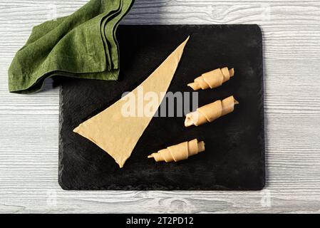 Rohe Teigstücke auf schwarzem Schieferbrett, in Croissant gerollt, Draufsicht Stockfoto