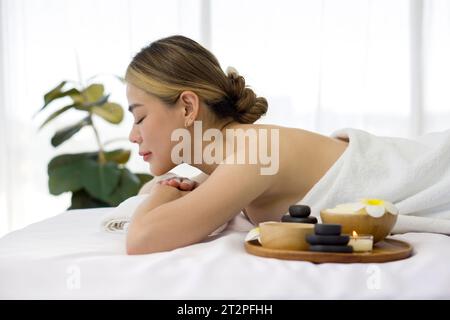 Eine ruhige Frau, die sich gemütlich in einem entspannenden Spa-Ambiente zurücklehnt, umgeben von Elementen, die Ruhe fördern. Ganzheitliches Luxus-Wellness-Erlebnis. Stockfoto