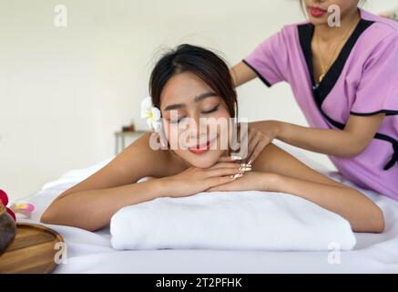 Eine professionelle Masseurin gibt einer entspannten Frau, die mit weichen Handtüchern bedeckt ist, aufmerksam eine therapeutische Massage. Atmosphäre in ruhiger Atmosphäre in einem Spa. Stockfoto