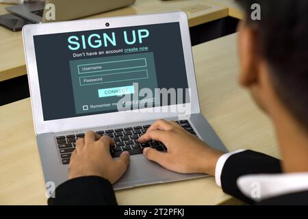 Ein fokussierter Geschäftsmann in schwarzem Anzug, der sich mit der Online-Erstellung seiner Identität beschäftigt und sich für ein Konto auf seinem Laptop registriert. Digital Life Explora Stockfoto