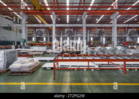 In der Blechfabrik werden Metallbleche und Stahlblechrollen auf den Boden gestellt. Großer Kran und Lkw befinden sich im Arbeitsbereich. Stockfoto