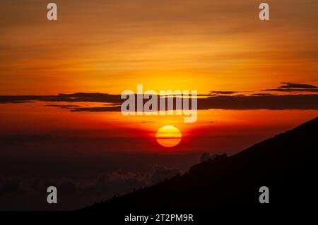 Nahaufnahme eines Sonnenaufgangs vom Mount Batur, mit der Sonne, die aus den Wolken auftaucht Stockfoto