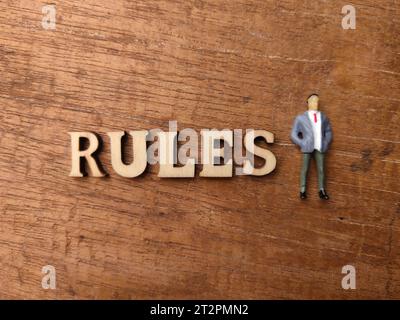 Hölzerne Wort- und Miniaturmenschen mit WORTREGELN auf hölzernem Hintergrund. Stockfoto