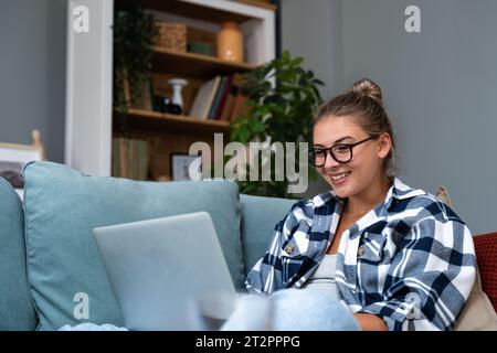 Junge erfolgreiche freie Unternehmerin, die auf dem Sofa liegt und von zu Hause aus auf dem Laptop arbeitet. Millennials Hipster-Frau, die im Netz surft Stockfoto