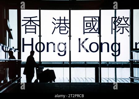 Passagier mit Gepäck und Trolley am Eingang zum internationalen Flughafen Chep Lak Kok, vor dem englischen und chinesischen Schild, Hong Kong, SAR, China Stockfoto