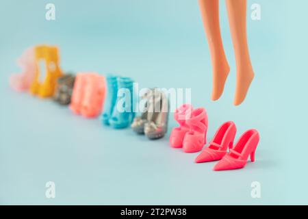 Plastikpuppenbeine in Spielzeugschuhen und viele verschiedene modische Schuhe auf rosa Hintergrund. Lernspiele für Kinder. Wechselschuhe g Stockfoto