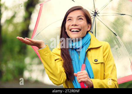 Herbstfrau glücklich nach Regen, die mit Regenschirm läuft. Weibliches Model, das am regnerischen Herbsttag fröhlich zum Himmel blickt und draußen einen gelben Regenmantel trägt Stockfoto