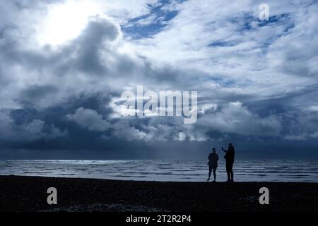 Worthing, Großbritannien. Oktober 2023. UK. Samstag, 21. Oktober 2023. Ein Paar fotografiert die Wolkenbildung, wenn die Sonne bei Wetter an der West Sussex Küste am East Beach, Worthing, bricht. Während Sturm babet extremes Wetter und Regen über das Land schiebt, werden die stürmischen Wolken für einen kurzen Moment am Morgen hinter einem blauen Himmel über der Küste von Sussex beleuchtet. Foto von Julie Edwards Credit: JEP/Alamy Live News Stockfoto