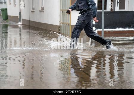 Polizist, der durch das Wasser einer überfluteten Straße bei Hochwasser der Trave in der Altstadt von Lübeck an der Ostsee in Deutschland läuft, c Stockfoto