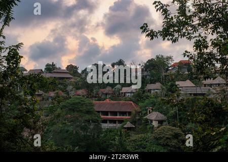 Erleben Sie die bezaubernde goldene Stunde in Ubud, Indonesien, wo die Sonne ein warmes, gelbliches Leuchten ausstrahlt und die Häuser inmitten üppiger Bäume beleuchtet Stockfoto