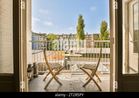 Ein Balkon mit zwei Stühlen und einem Tisch in der Mitte, mit Blick auf den Hof von einer offenen Tür Stockfoto