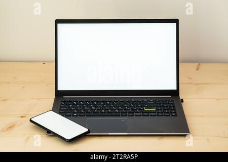 Foto von Laptop und Smartphone auf Holzschreibtisch mit weißem Bildschirm. Stockfoto