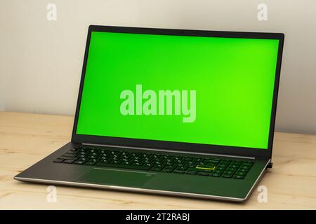 Ein Foto eines Laptops auf einem Holzschreibtisch mit einem grünen Bildschirm. Stockfoto