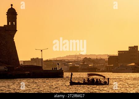 Die maltesische Dghajsa (ähnlich einer Gondel) transportiert Passagiere zwischen Valletta und Birgu in Malta, während die Sonne untergeht Stockfoto
