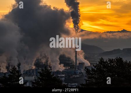 Rauch und Dampf aus der Fabrik mit Kamin und buntem Himmel im Hintergrund. Stockfoto