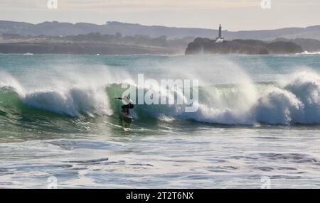 Ein Surfer mit Mouro Island am Eingang zur Bucht mit starken Wellen an einem sonnigen Herbstmorgen Sardinero Santander Cantabria Spanien Stockfoto