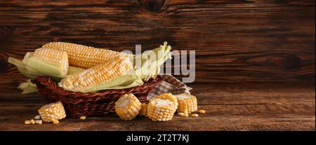 Frische Maiskolben im Korb auf hölzernem Hintergrund mit Platz für Text Stockfoto