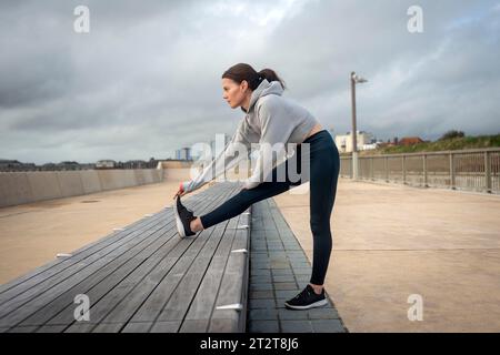 Sportliche Frau, die draußen Beindehnungsübungen macht. Workout im Freien. Stockfoto