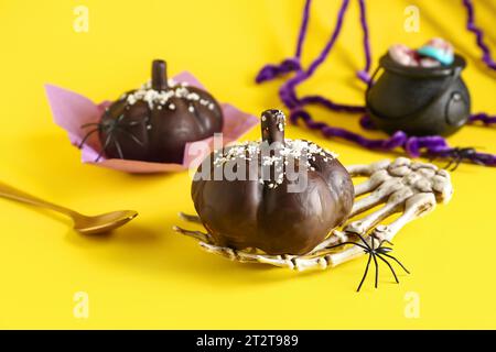 Köstliche Schokoladenkuchen, Skelett Hand und Spinne für Halloween Feier auf gelbem Hintergrund, Nahaufnahme Stockfoto