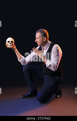 Reifer Schauspieler mit Schädel auf dunklem Hintergrund Stockfoto