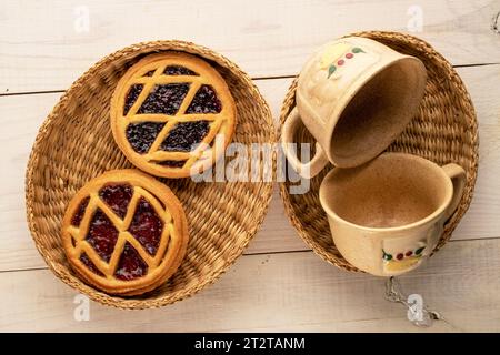 Zwei Shortbread Plätzchen mit Marmelade mit Strohplatten und zwei Tassen auf einem Holztisch, Makro, Draufsicht. Stockfoto