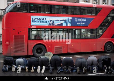 Muslimische Männer beten neben einem Londoner Bus, während pro-palästinensische Demonstranten die zweite Woche in Folge nach den Angriffen der Hamas auf Israel am 21. Oktober 2023 in London durchmarschieren. Die Met Police hat geschätzt, dass 100.000 an dem Protest durch die Hauptstadt teilgenommen haben, das zweite Massenereignis in einer Woche. Stockfoto