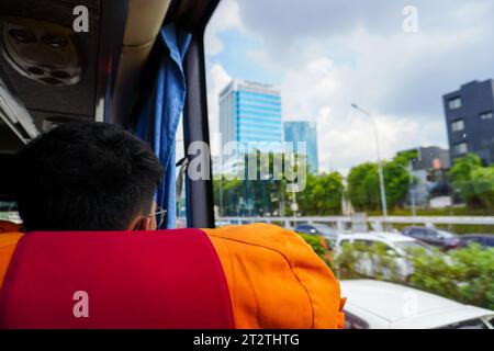 Ein Mann, der aus dem Fenster eines fahrenden Busses blickt, ist von der beeindruckenden Stadtlandschaft der Wolkenkratzer und befahrenen Straßen fasziniert Stockfoto